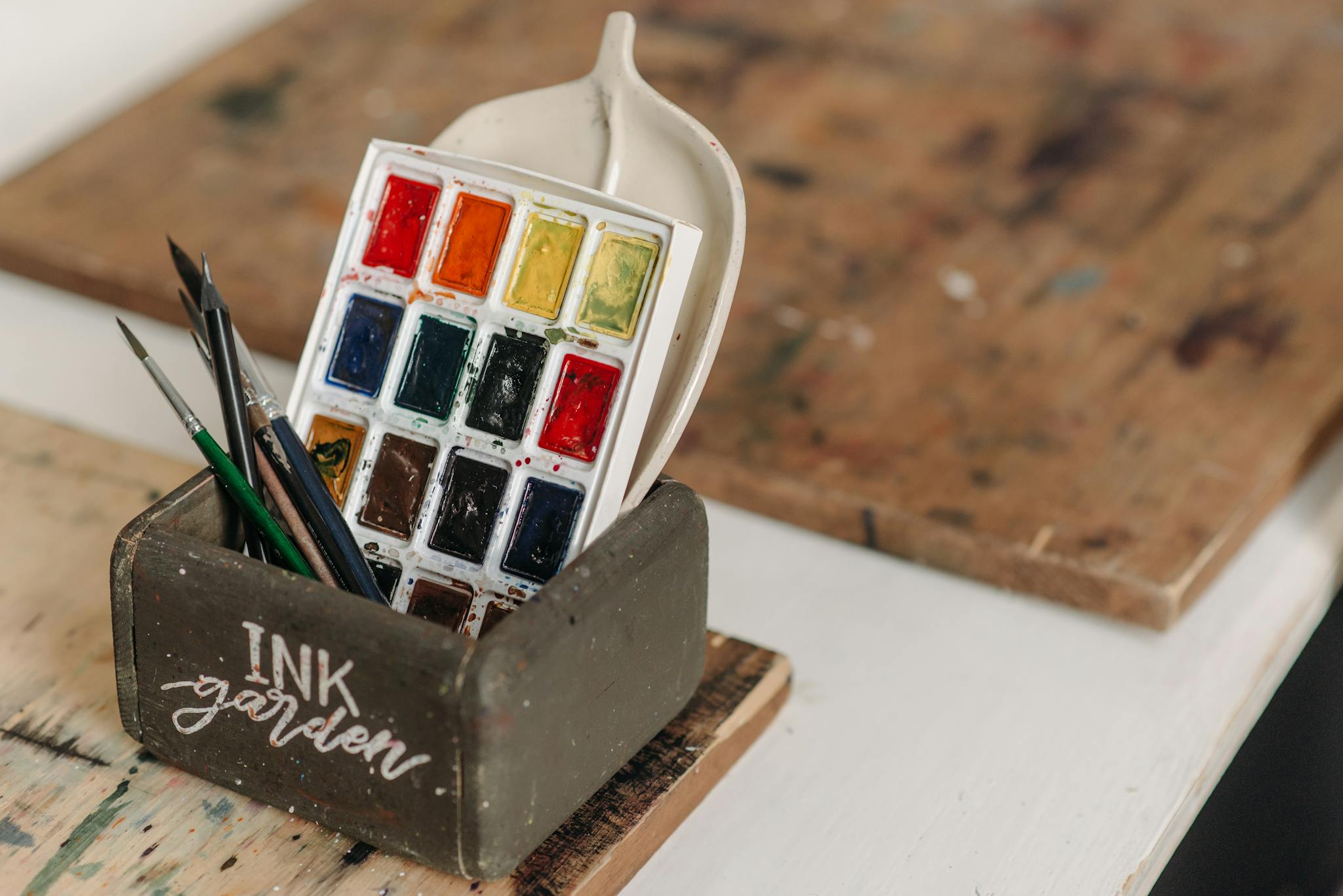 Watercolor paints and brushes arranged on a wooden table in a creative workshop.